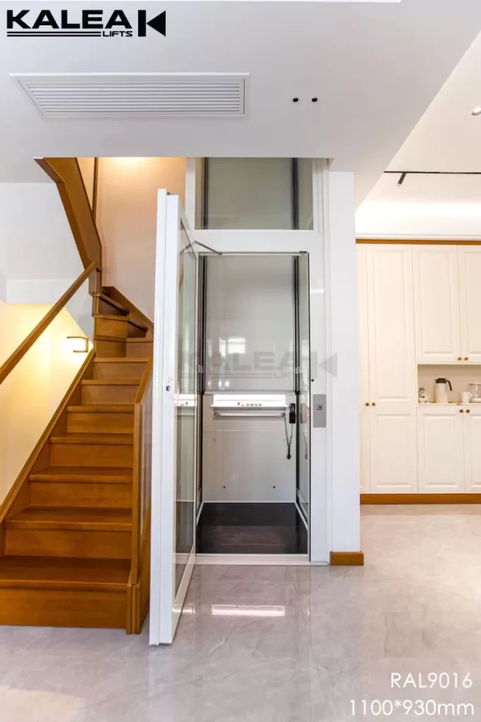 Lift rumah Kalea KLASSIC dengan panel putih dan pintu kaca terpasang di samping tangga kayu rumah